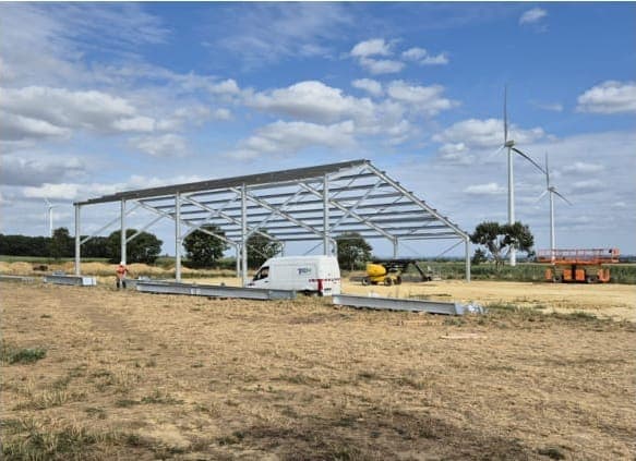 Charpente métallique d'ombrière en cours de montage par TP COM, éoliennes en arrière-plan